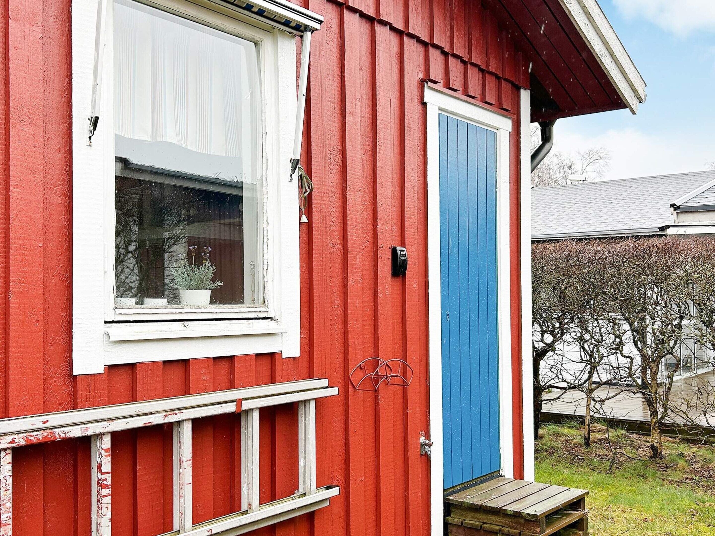 En rød bygning med et hvidt vindue, en blå dør og en lille træterrasse.