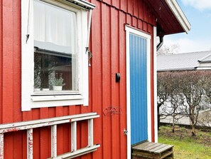 Egy piros épület, fehér ablakokkal, kék ajtóval és egy kis, fából készült verandával.