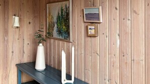 A wooden wall with a painting, a framed picture, a white vase, and two white candles on a blue bench. - 6 Person Holiday Home in Laholm (Skummesloevsstrand)