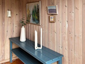 A wooden wall with a painting, a framed picture, a white vase, and two white candles on a blue bench. - 6 Person Holiday Home in Laholm (Skummesloevsstrand)