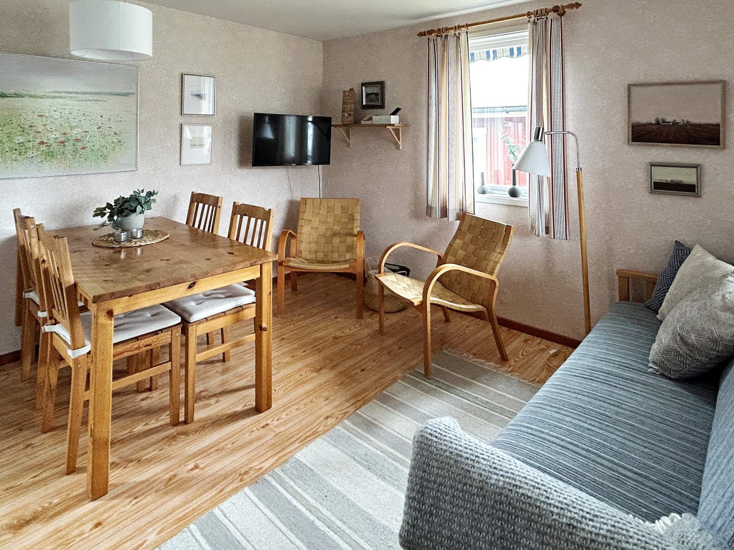 A living room with a wooden dining table, chairs, a sofa, a television, and a window with curtains.