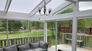 A sunroom with a sofa and table, large windows, and a view of a deck and yard. - 4 Star Holiday Home in Malmkoping (Malmkoping)