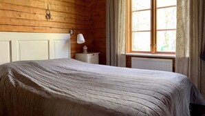 A wooden cabin bedroom with a bed, a nightstand, a lamp, and a window with curtains. - 4 Star Holiday Home in Malmkoping (Malmkoping)