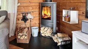 A cozy cabin interior with a wood-burning stove, a sofa, a TV, and a fireplace mantel with a basket and a kettle. - 4 Star Holiday Home in Malmkoping (Malmkoping)