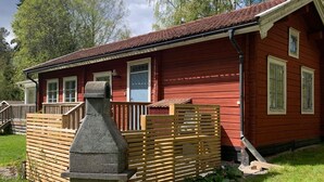 A red wooden cabin with a stone chimney, wooden deck, and a fenced garden area. - 4 Star Holiday Home in Malmkoping (Malmkoping)