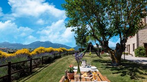 An outdoor dining table set with plates, a bottle of wine, and a pitcher, overlooking a garden with flowers and a mountain view. - Relaxing Countryside Stay (Cagli)