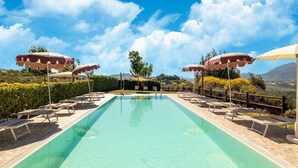 A rectangular swimming pool with lounge chairs and umbrellas, surrounded by a wooden deck and a landscaped garden with a view of distant hills. - Relaxing Countryside Stay (Cagli)