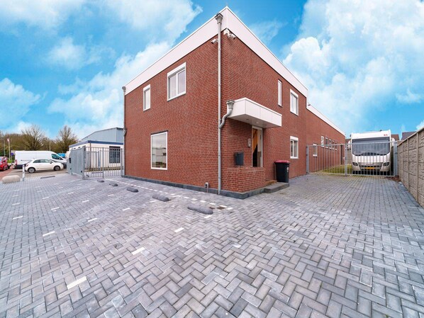 A red brick building with a paved driveway and a gated entrance. - Serene Stay With All You Need (Landgraaf)