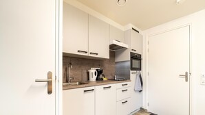 A modern kitchen with white cabinets, a wooden countertop, a kettle, a coffee maker, and a black and white striped towel hanging on the wall. - Serene Stay With All You Need (Landgraaf)