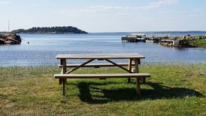A picnic table by a calm body of water with a dock and a small island in the distance. - 5 Person Holiday Home in Stromstad (Stromstad)