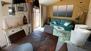 Una sala de estar acogedora con techo de madera, un sofá verde, un sillón blanco y una mesa de comedor con sillas.