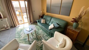 Una sala de estar con un sofá verde, sillones blancos, una mesita y vistas al exterior a través de un ventanal.