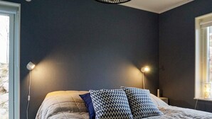 Un dormitorio con una cama, dos lámparas de noche, una ventana y una mesita.