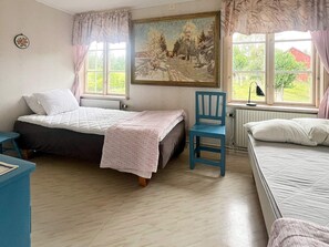 Ett sovrum med två sängar, en stol, ett skrivbord och en tavla på väggen.