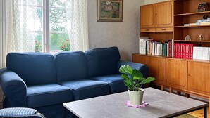 A living room with a blue sofa, a small table with a plant, a bookshelf, and a patterned rug. - 5 Person Holiday Home in Mariannelund (Mariannelund)