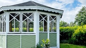 Un belvédère aux couleurs extérieures vertes et aux bordures blanches, entouré d’un jardin bien entretenu.