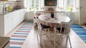 A kitchen with white cabinets, a dining table with chairs, and a window with floral curtains. - 5 Person Holiday Home in Mariannelund (Mariannelund)