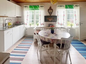 Een keuken met witte kastjes, een eettafel met stoelen en een raam met bloemen gordijnen.