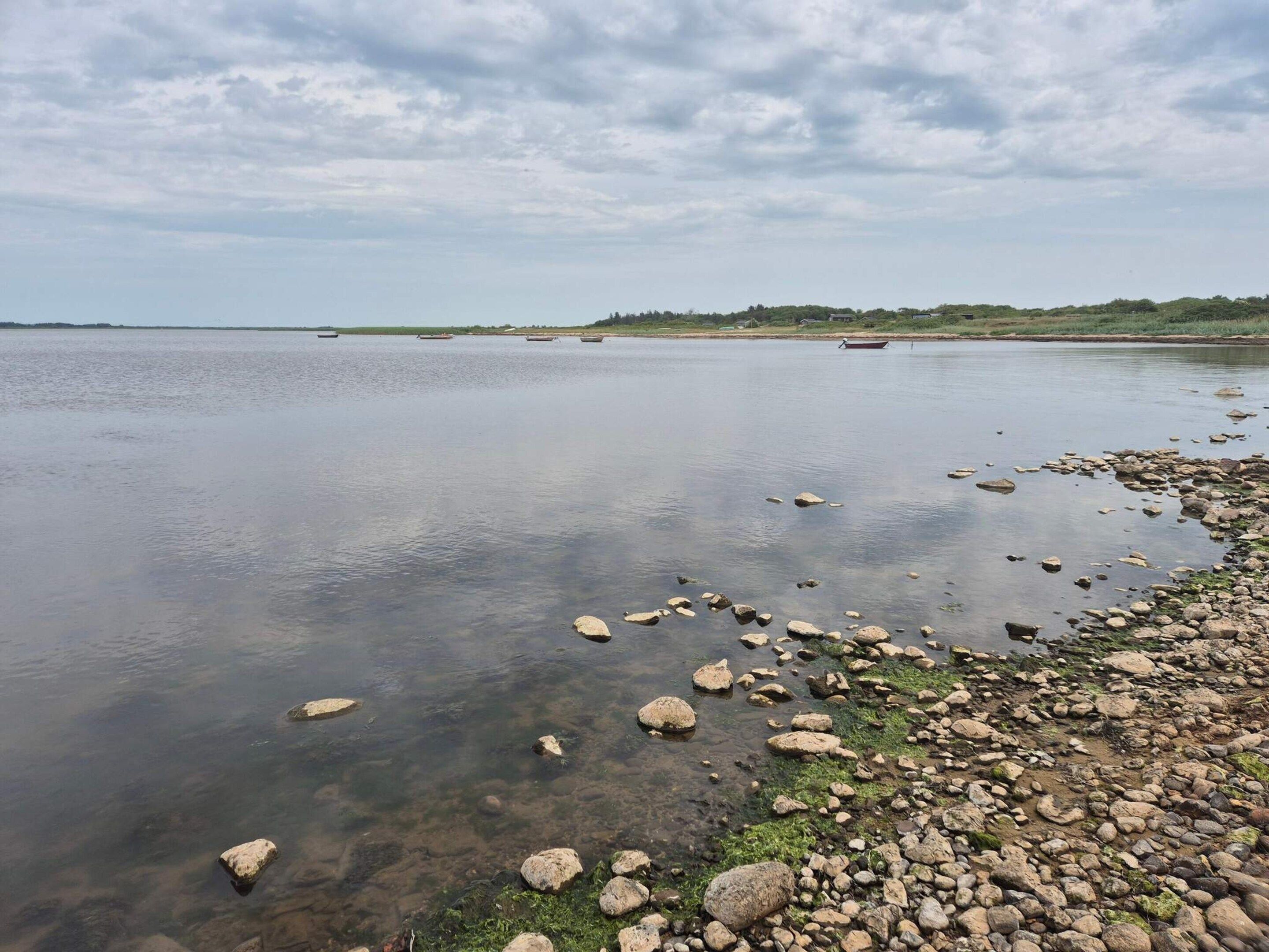 A calm lake with a rocky shoreline and boats in the distance.
