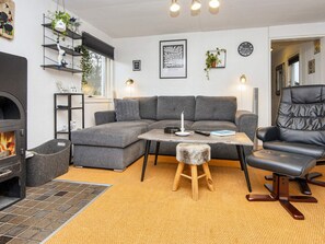 A cozy living room with a sectional sofa, a black leather chair, a small wooden stool, a fireplace, and a wall-mounted shelf with plants. - 5 Person Holiday Home in Tarm (Tarm)