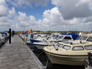 Un puerto deportivo con varias embarcaciones amarradas, un muelle de madera y un cielo nublado.
