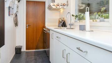 Una cocina compacta con puerta de madera, armarios blancos, un lavamanos de acero inoxidable y una ventana con plantas.