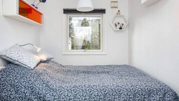 Un dormitorio con una cama, una ventana, una lámpara colgante y una estantería con flores.