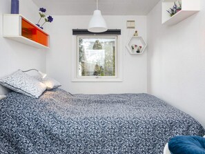 Un dormitorio con una cama, una ventana, una lámpara colgante y una estantería con flores.