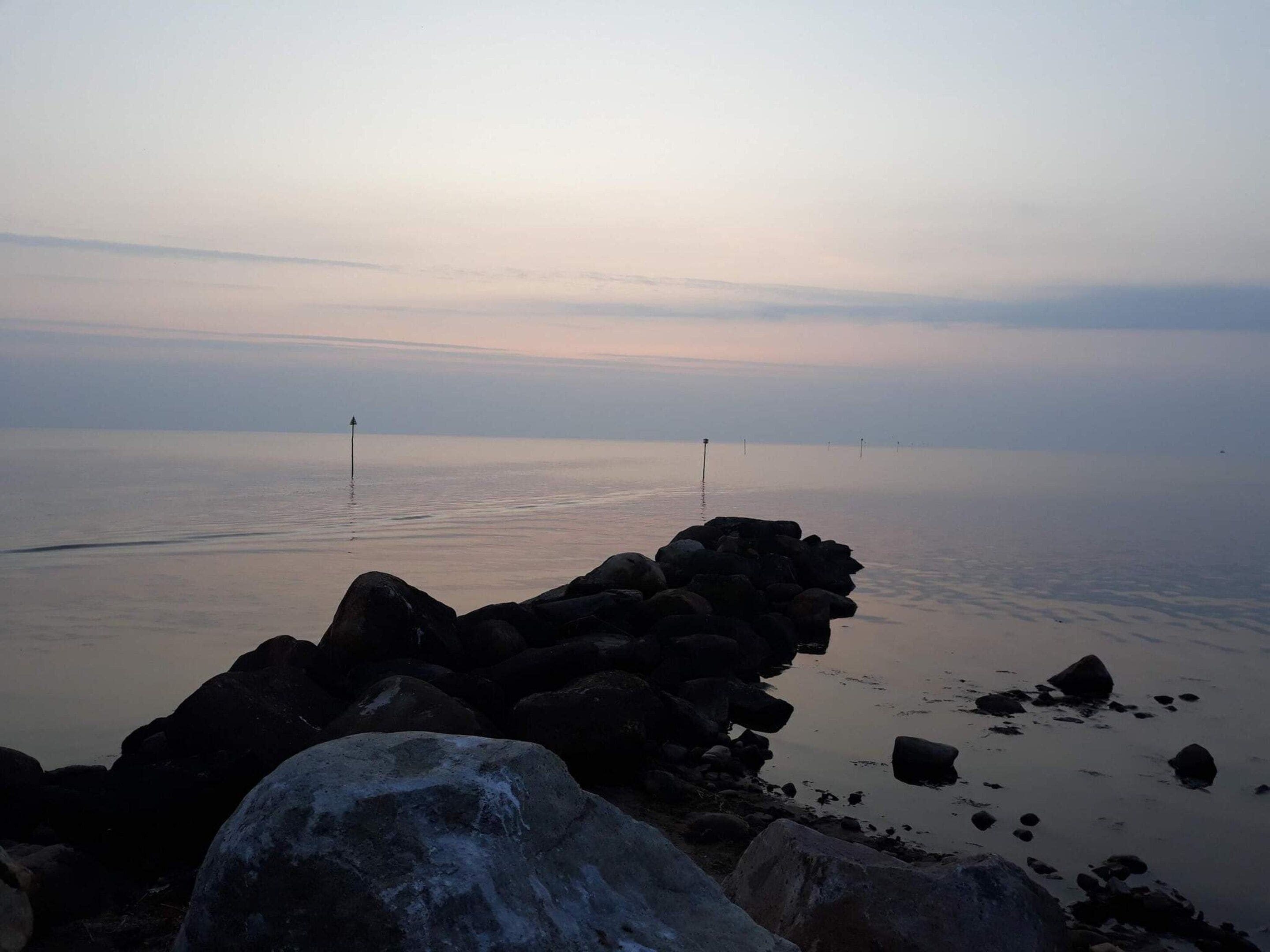 A calm sea with a rocky breakwater in the foreground.