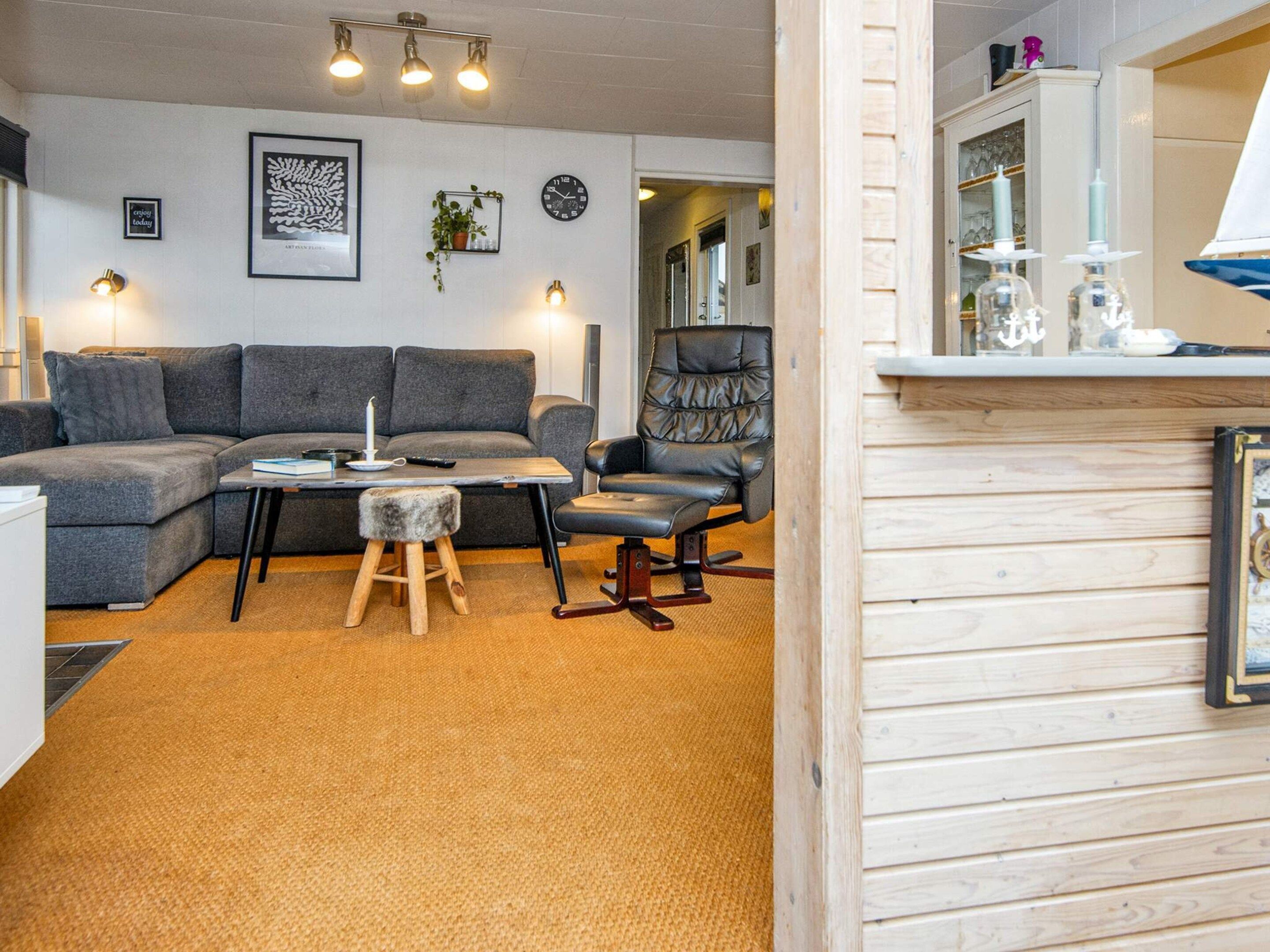 Una sala de estar moderna con un sofá seccional gris, una mesa de centro de madera, un taburete pequeño, un sillón de cuero negro y un mueble de madera con cristalería.