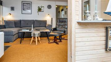 Una sala de estar moderna con un sofá seccional gris, una mesa de centro de madera, un taburete pequeño, un sillón de cuero negro y un mueble de madera con cristalería.
