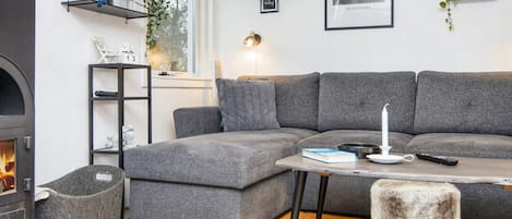 A modern living room with a grey sectional sofa, a small table with a candle, a fireplace, and a wall-mounted shelf with plants.