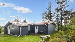 A two-story cabin with a red-tiled roof, a small porch, and a garden with various plants and a bench. - 5 Person Holiday Home in Tarm (Tarm)