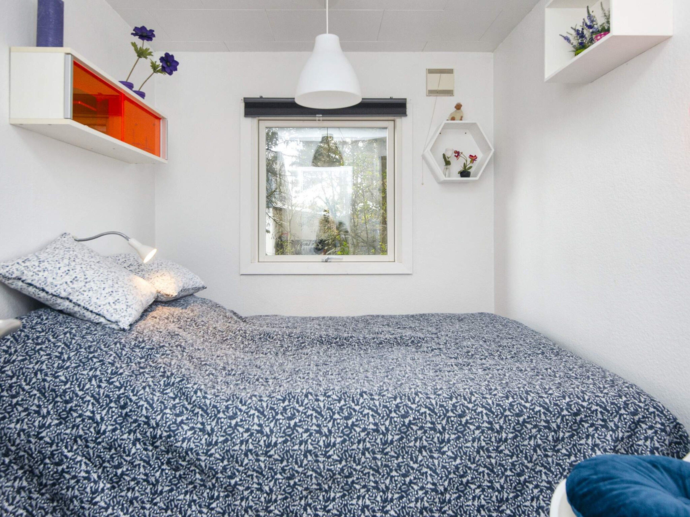Un dormitorio con una cama, una ventana, una lámpara colgante y una repisa con flores.