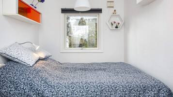 Un dormitorio con una cama, una ventana, una lámpara colgante y una repisa con flores.
