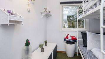 Una habitación pequeña con literas, una mesita, un ventanal y un coche de juguete rojo.