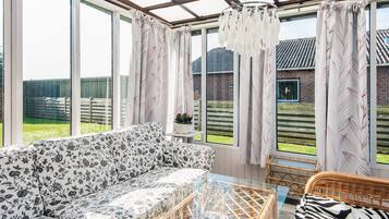 Ein Wintergarten mit einer Couch, Korbmöbeln und einem Glastisch.