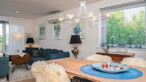 Una sala de estar moderna con comedor, con una araña, obras de arte en las paredes y vistas a zonas verdes.