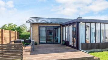 Ein modernes Haus mit einer Holzterrasse, einem Wintergarten aus Glas und einer Ziegel Fassade.