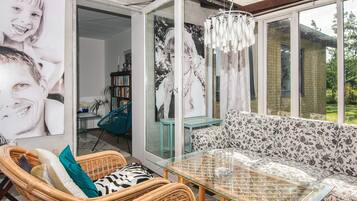 Ein Zimmer mit Glastisch, Korbmöbeln, einem gemusterten Sofa und einem großen Fenster.
