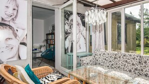 Un espacio de sala acogedor con una mesa de vidrio, sillas de mimbre, un sofá estampado y una estantería.