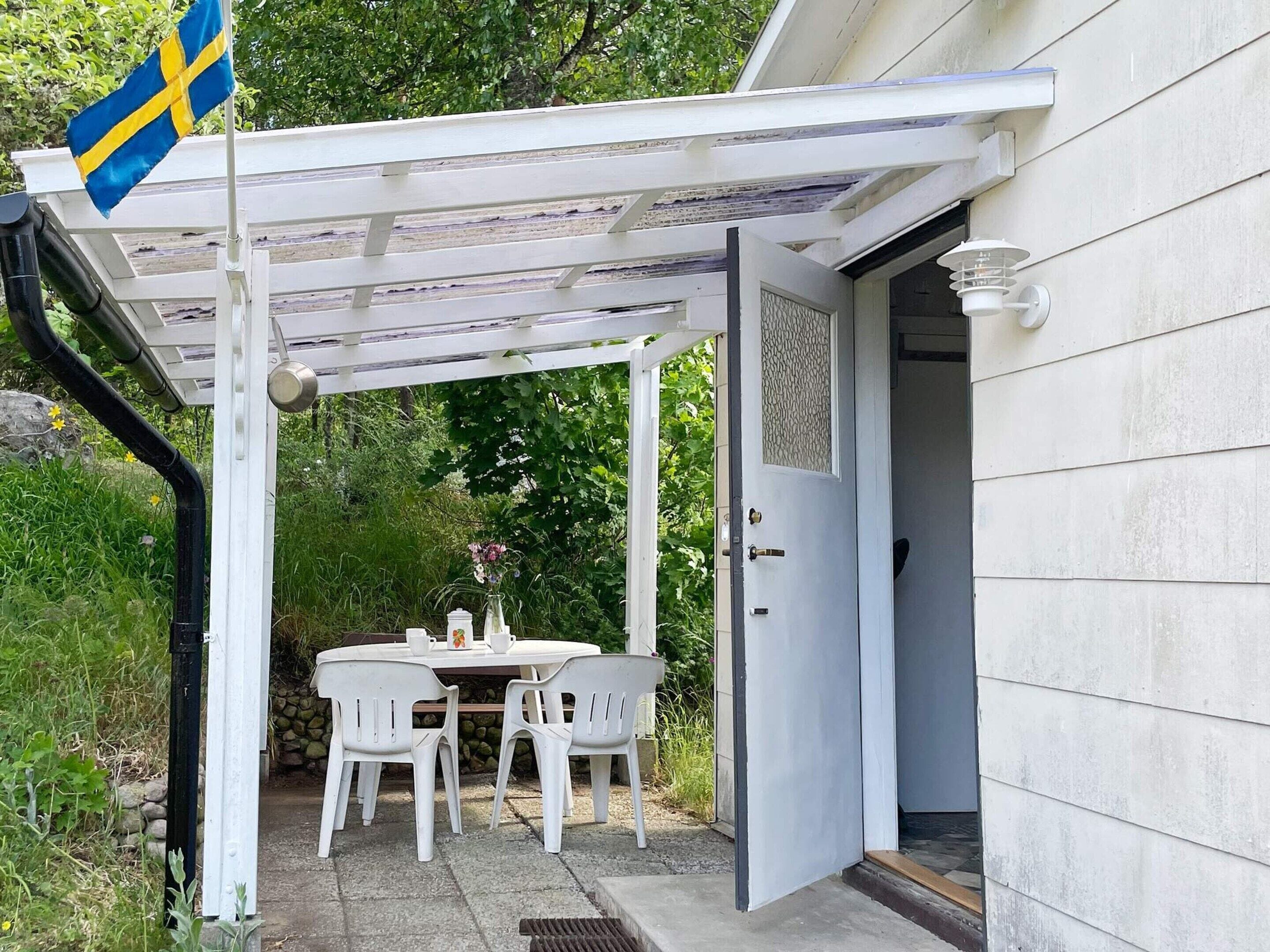 Um alpendre coberto com mesa, cadeiras, uma bandeira e uma porta que dá para uma casa.