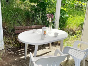 A white outdoor table with a bench, surrounded by greenery and a stone wall. - 4 Person Holiday Home in Asarum (Asarum)