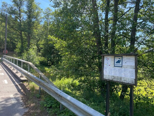 Une glissière métallique au bord d’une route, un panneau de signalisation indiquant un arrêt obligatoire et un panneau en bois avec du texte et une carte.