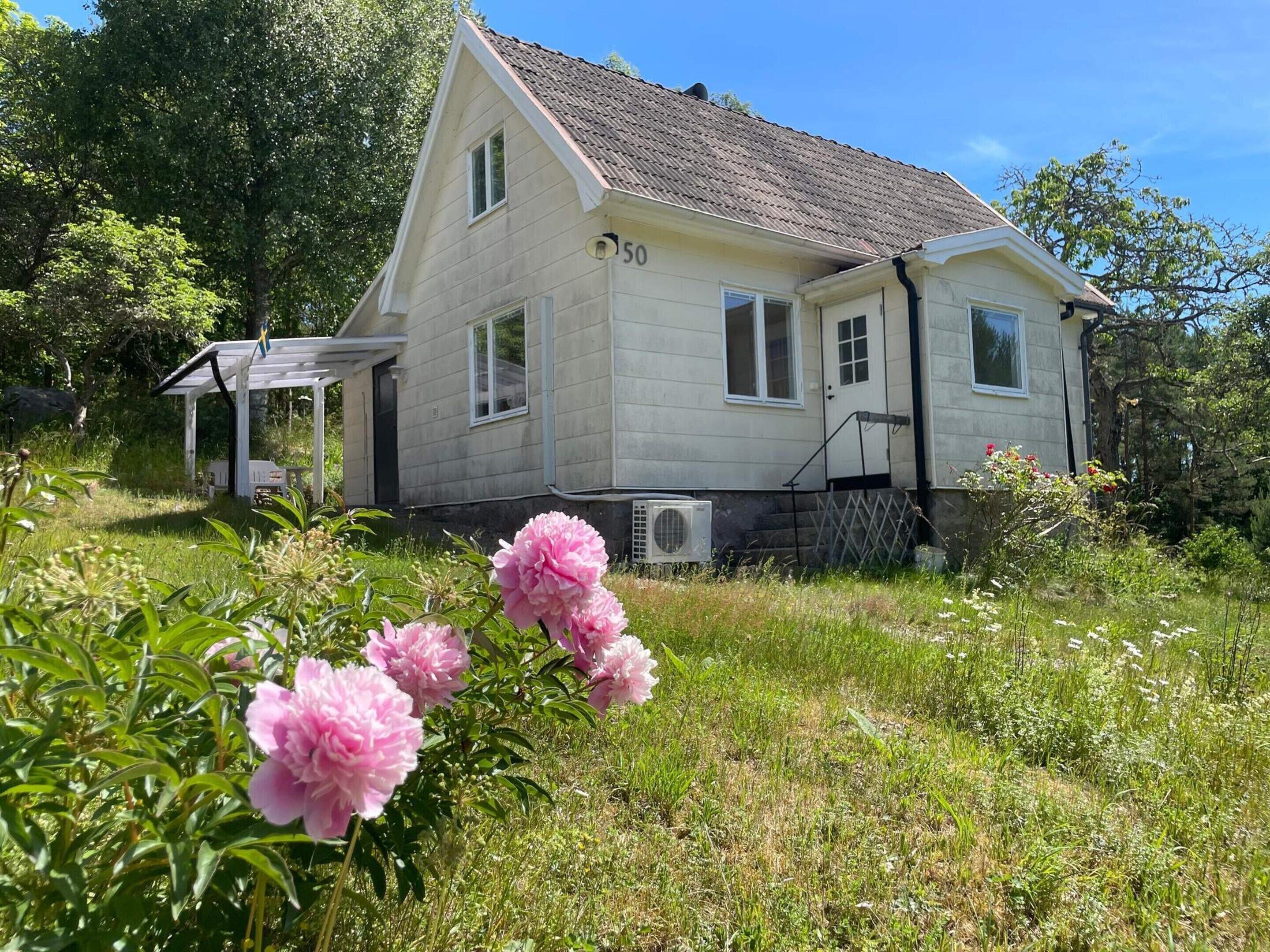 Ett tvåvåningshus med nummer 50 på sidan, en veranda och en trädgård med rosa blommor.