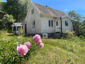 A two-story house with a number '50' on the side, a porch, and a garden with pink flowers. - 4 Person Holiday Home in Asarum (Asarum)