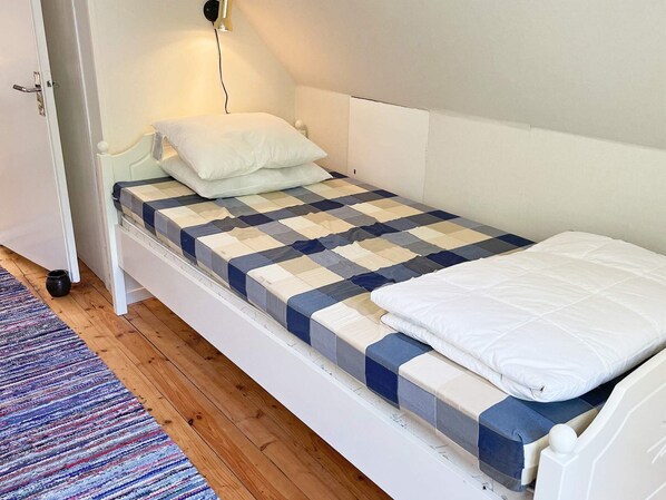 Una cama individual con una colcha a cuadros, una almohada blanca y una mesita de noche con una lámpara.