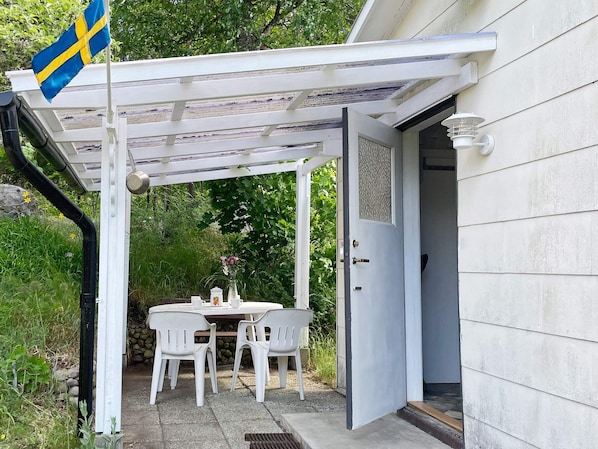 Une terrasse couverte avec une table et des chaises, un drapeau et une porte donnant sur un bâtiment.