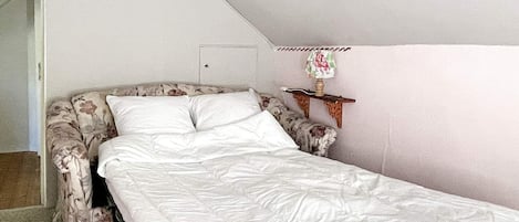 Una cama individual con colchón blanco y cabecera estampada en una habitación con techo inclinado.