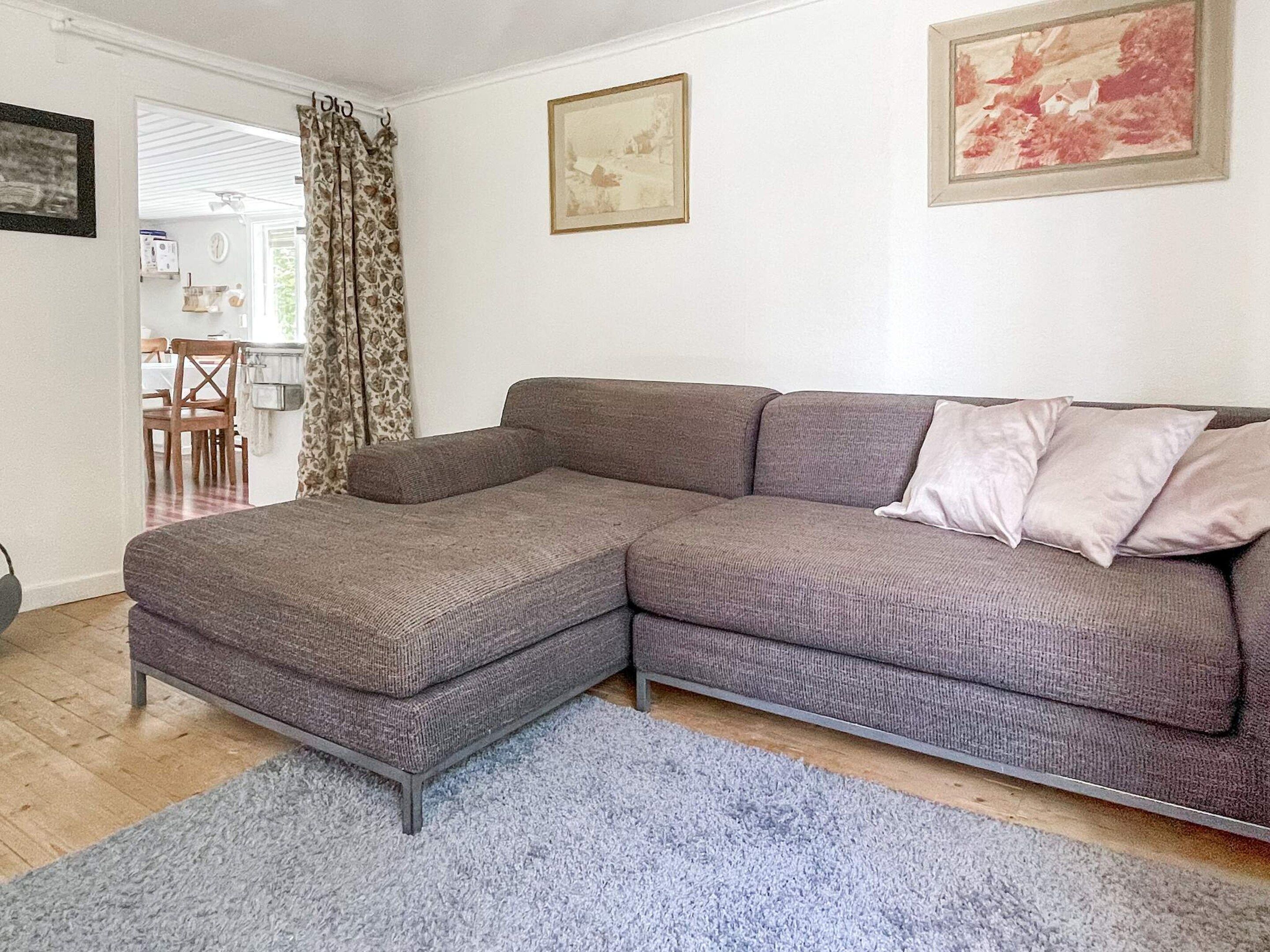 A living room with a grey sectional sofa, a blue rug, and a dining area in the background.